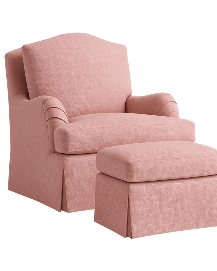 The Balmoral Chair, upholstered in a blush pink fibregaurd fabric, featuring a high back, pleated arms, deep seat cushion, and a tailored skirted base.
