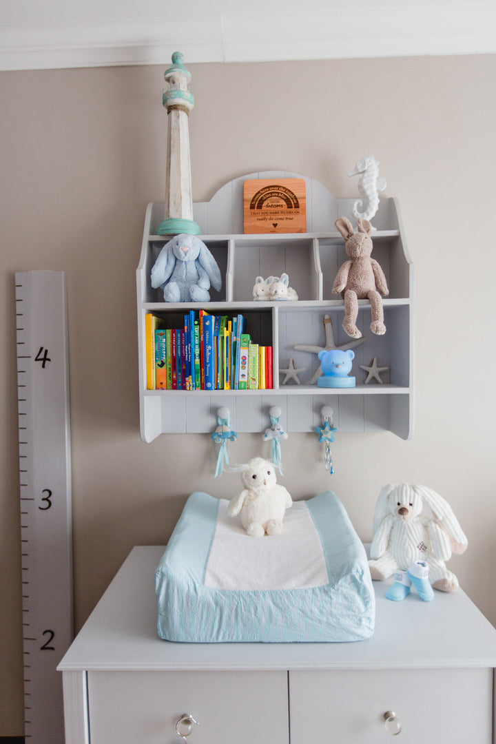 Grey Lyra wall shelf with open cubbies, pigeon holes, tongue-and-groove detail and three rounded hooks, styled for nursery or kids’ room
