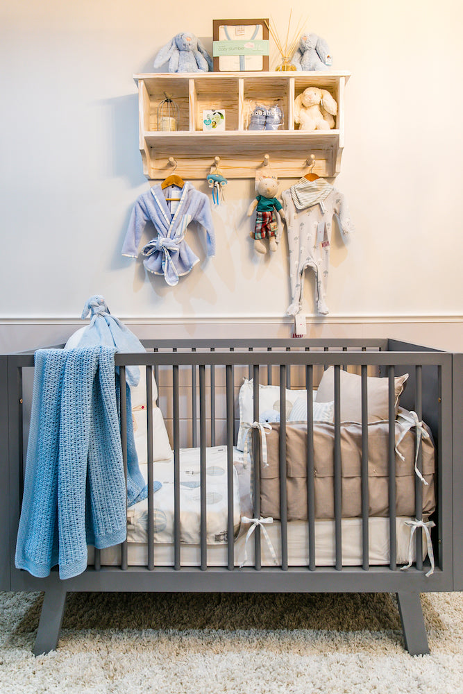 Distressed white Orchid wall shelf with four cubbies and three hooks, styled with baby clothes and toys, ideal for nursery storage
