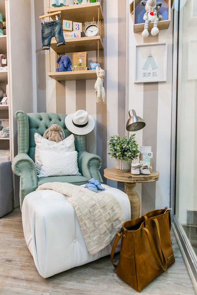 Sebastian Feeding Chair in green velvet upholstery, styled in a modern nursery with buttoned wingback design, studded arms, and Queen Anne legs, paired with a white ottoman and cosy décor.
